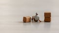 A miniature man relaxing next to a stacked box.